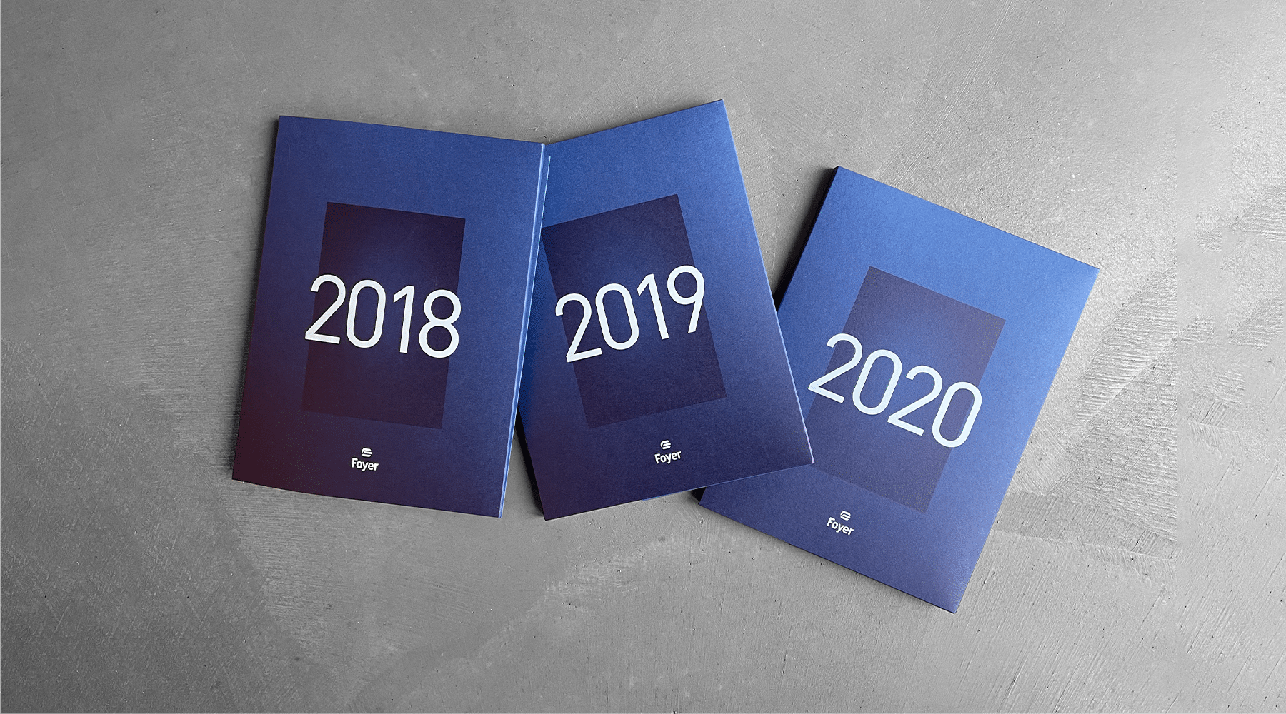 Trois rapports annuels de Foyer avec des couvertures bleues disposés en éventail, chacun portant les années 2018, 2019, et 2020 en grand format sur le devant.