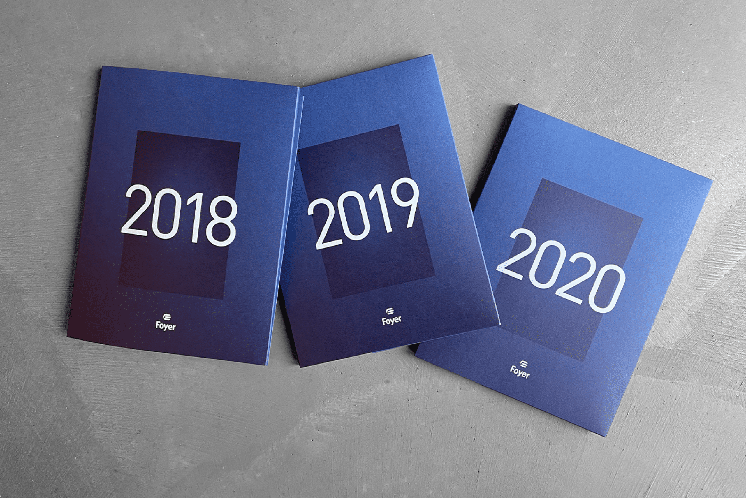 Trois rapports annuels de Foyer avec des couvertures bleues disposés en éventail, chacun portant les années 2018, 2019, et 2020 en grand format sur le devant.