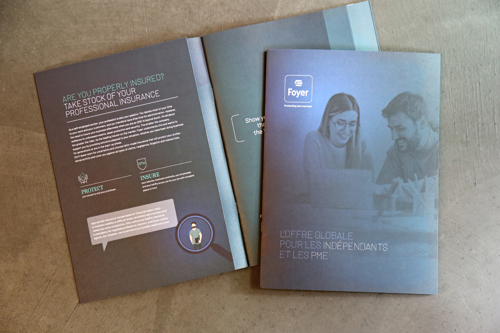 Deux brochures professionnelles de Foyer ouvertes et empilées; une affiche du texte sur l'assurance professionnelle en anglais et l'autre montre une image de deux professionnels travaillant ensemble avec le titre 'L'offre globale pour les indépendants et les PME' en français.
